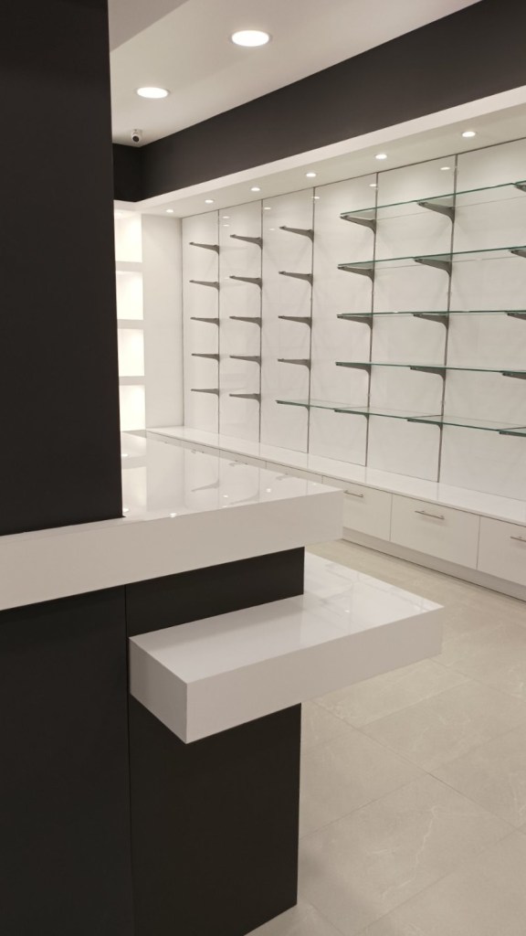 Ολοκληρωμένος εξοπλισμός μεγάλου φαρμακείου με λευκό γυαλιστερό ακρυλικό, ανθρακί λεπτομέρειες, κεντρικό πάγκο εργασίας και ενσωματωμένες συρταριέρες - Kappawood